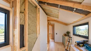 Parede de tiny house em construção com montantes de madeira, painéis isolantes entre as estruturas e cobertura inclinada com isolamento térmico parcialmente exposto.